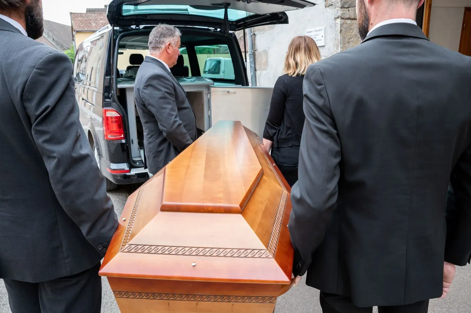 Équipe de porteurs en costume transportant un cercueil vers le véhicule funéraire.