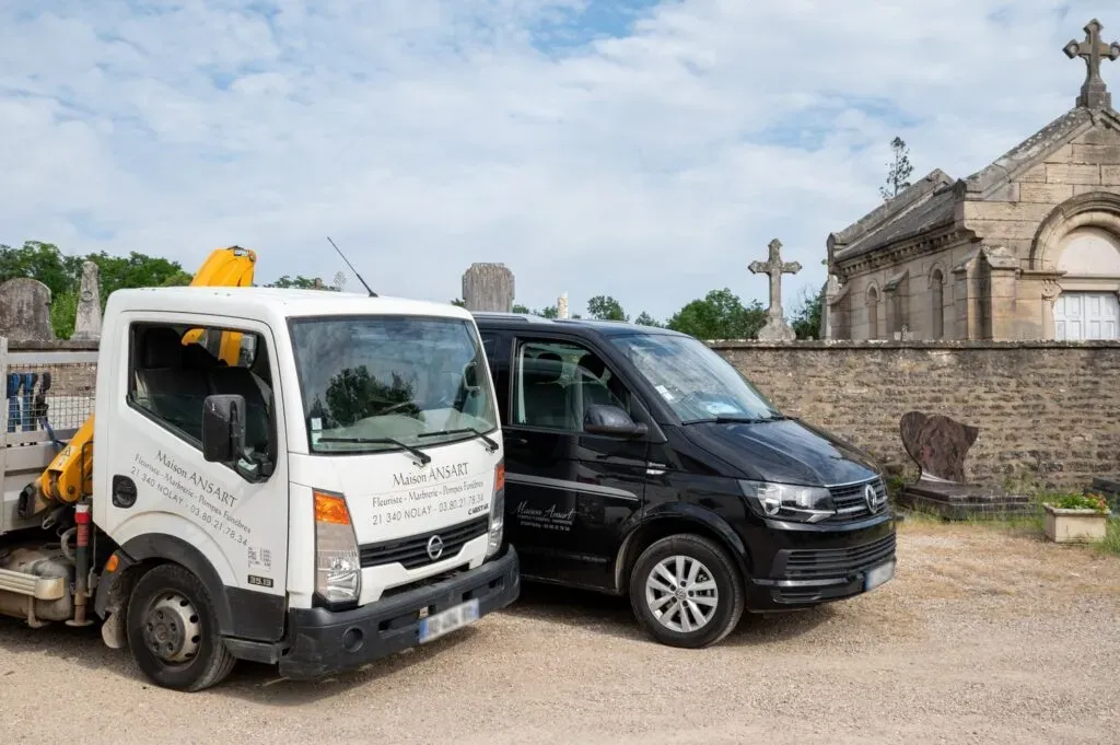 Camions d'intervention et corbillard de la Maison Ansart stationnés près d'un cimetière.