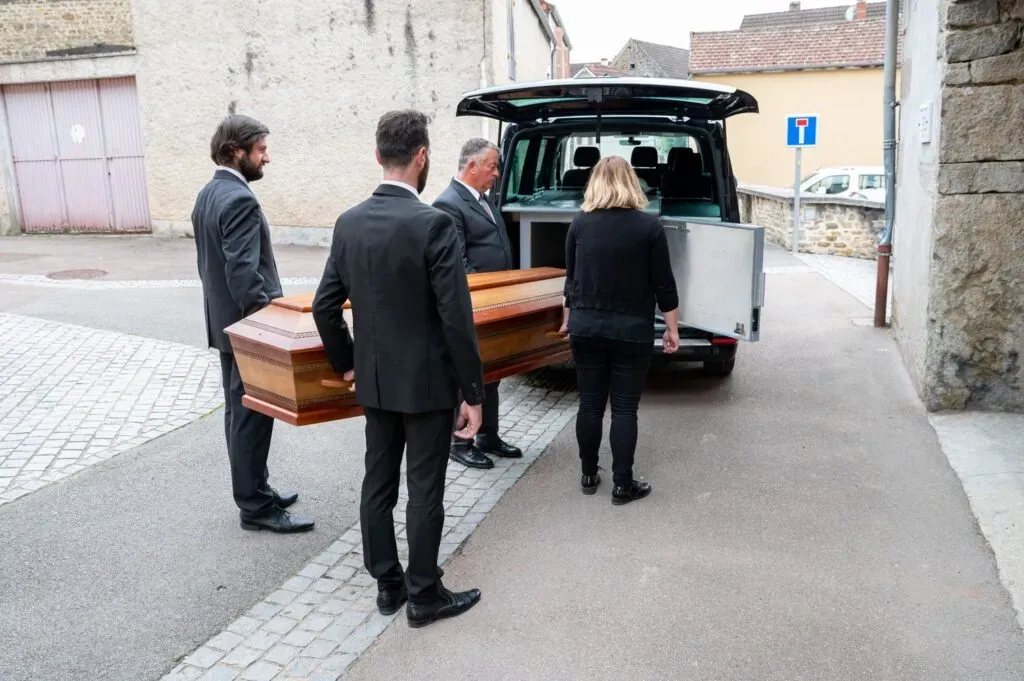 Porteurs en costume chargeant un cercueil en bois à l'arrière d'un corbillard.